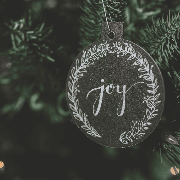 An ornament with the word JOY written across it hanging from a Christmas tree.