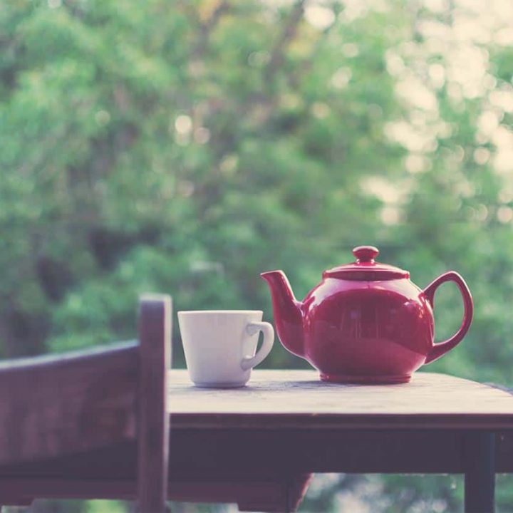 A tea pot and cup sitting on an outside table with a chair.