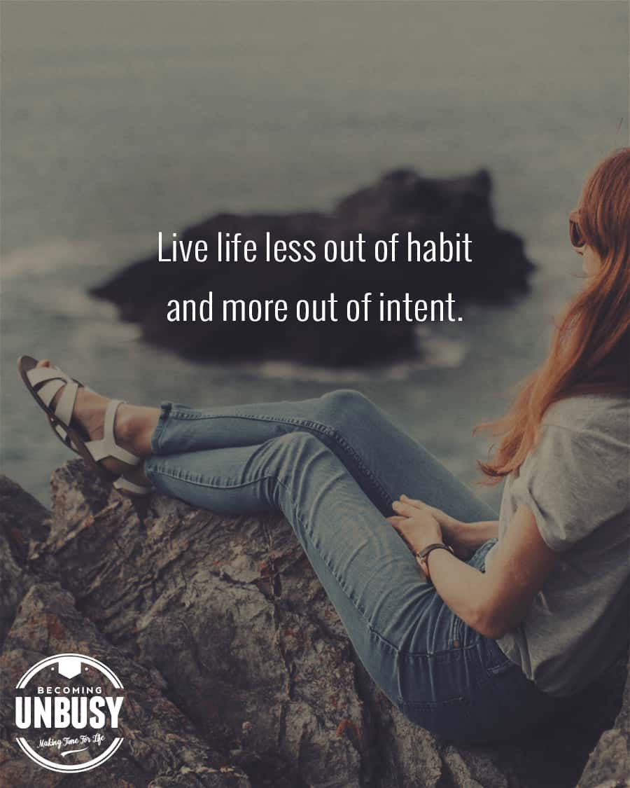 Woman sitting on the rocks with feet crossed looking at the ocean with the following quote on top "Live life less out of habit and more out of intent."