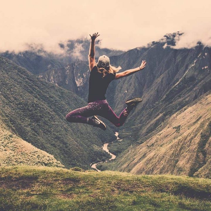 Photo of a woman jumping in the air with mountains in the distance.