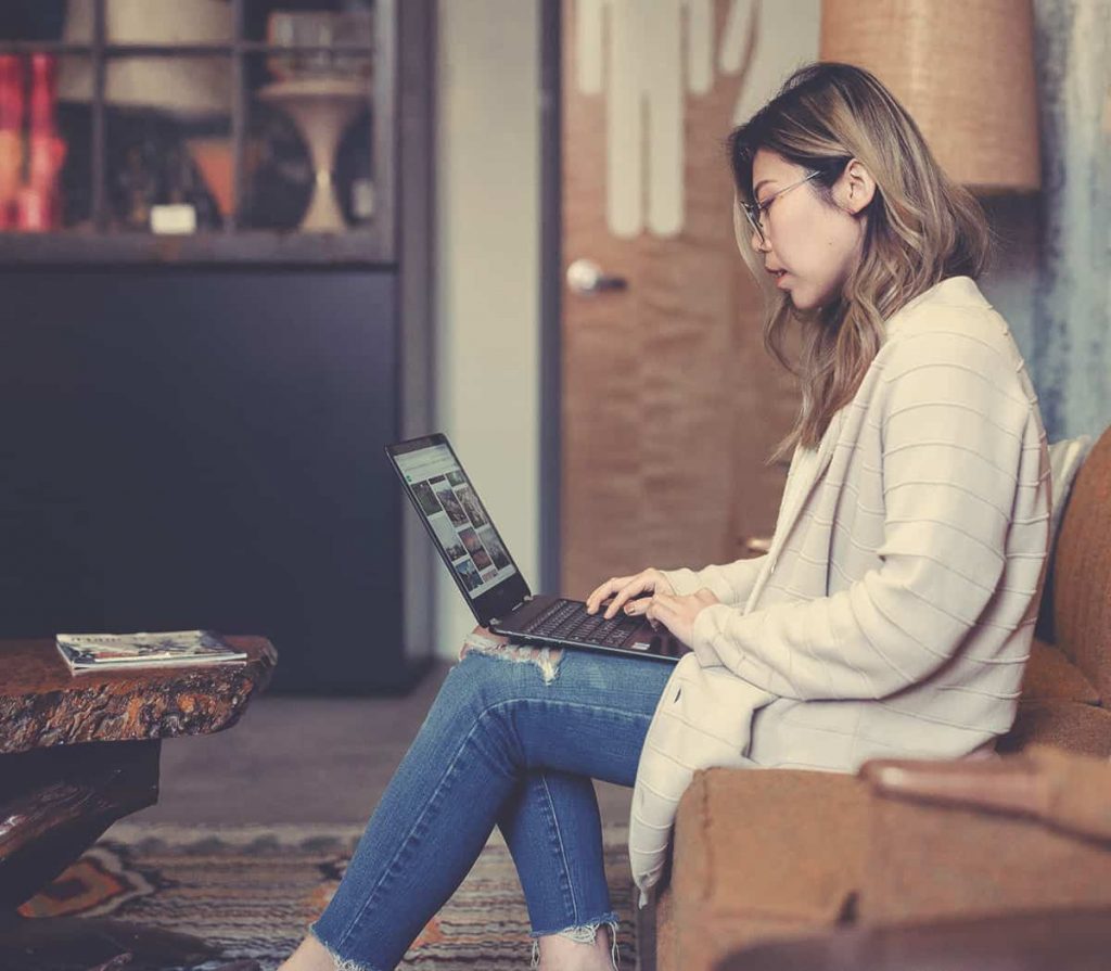 A woman sitting on a couch connecting with other members within the UnBusy Community using her laptop.