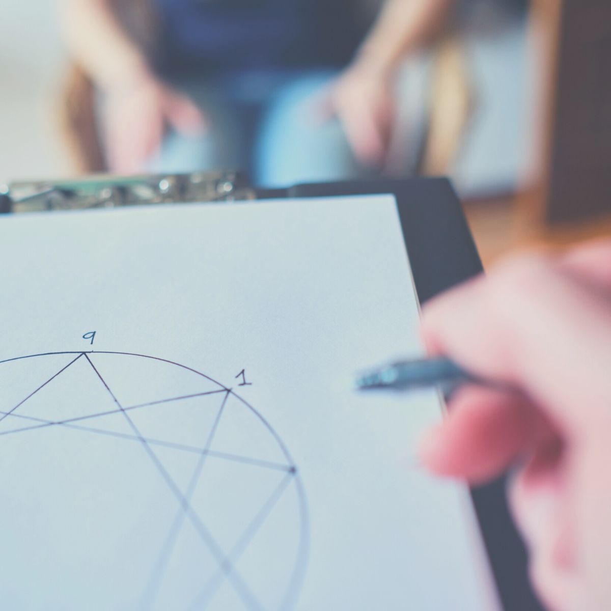 Person writing and doing an Enneagram test assessment on a clipboard with another person.