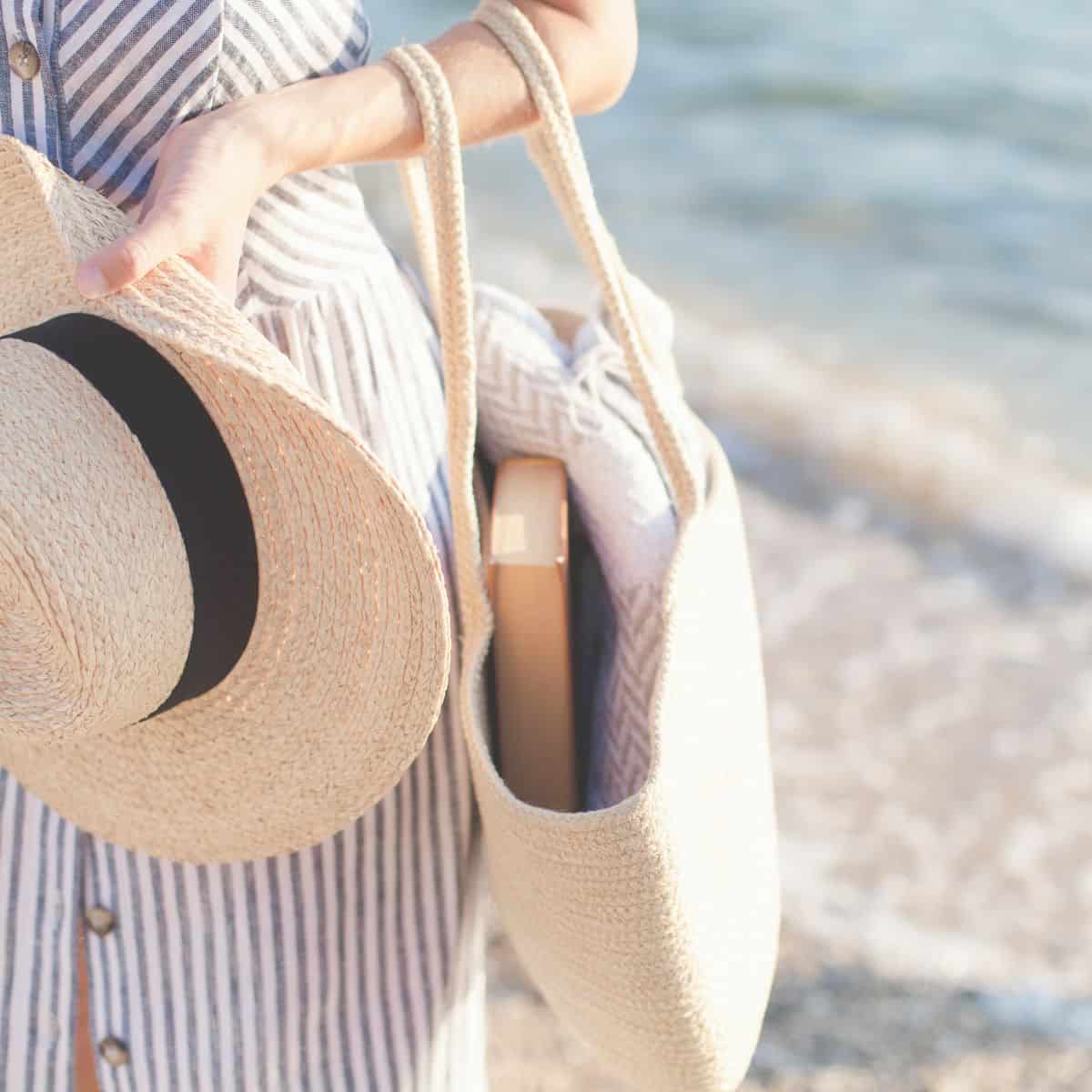 A modern kindred spirit carrying a straw beach hat and a canvas tote with the Anne of Green Gables book within it.