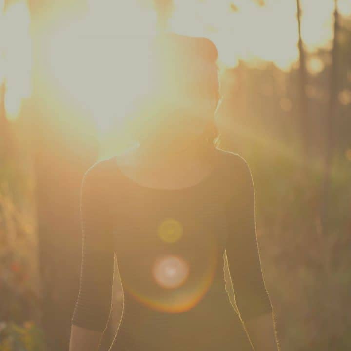 A woman walking in the woods in the morning, the early sunlight reflecting from her as if she is the light.