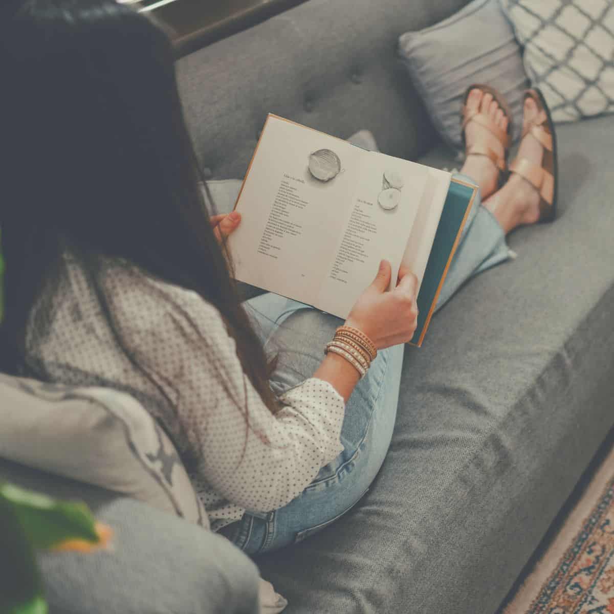 A woman enjoying the benefits of poetry while reading a poem collection on her sofa.