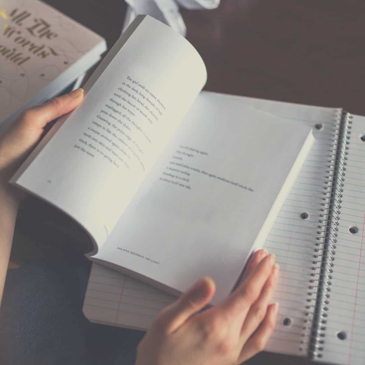 A woman reading poems about self at a table with a notebook and pen.