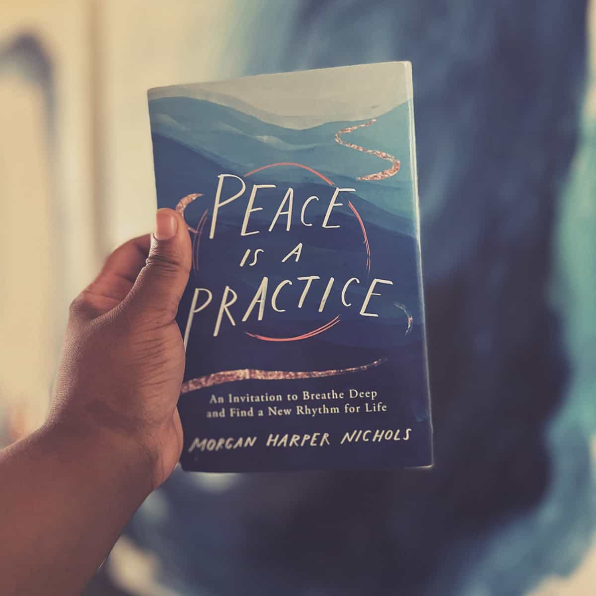 A woman's hand holding up a poetry book titled Peace Is A Practice: An Invitation to Breathe Deep and Find a New Rhythm for Life.