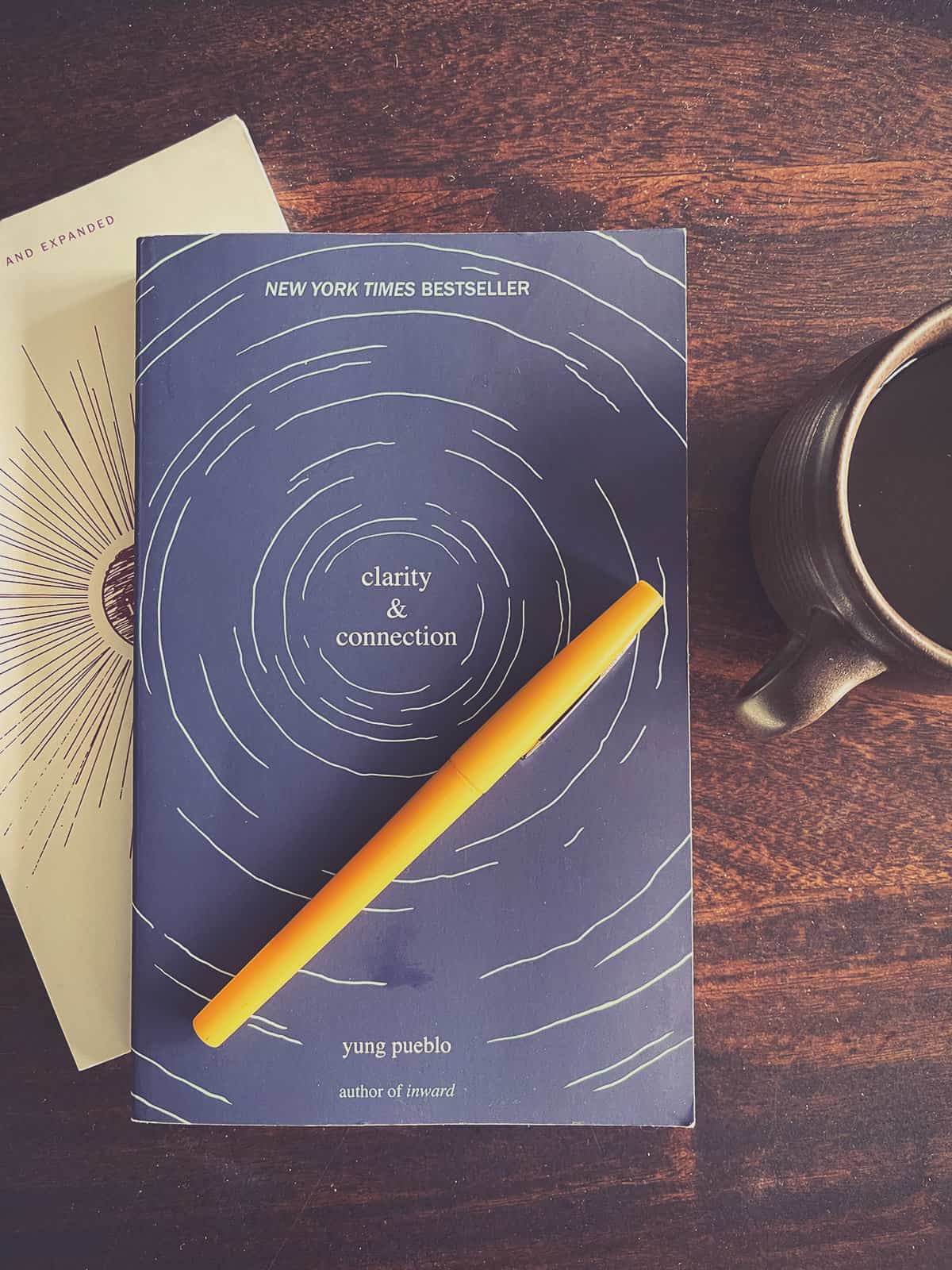 A poetry book entitled Clarity & Connection sitting on a table with a pen and cup of coffee.