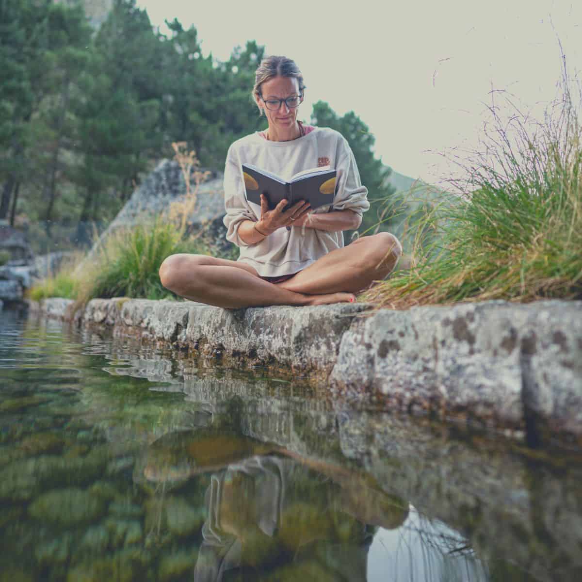 A woman who is trying to get comfortable being uncomfortable by reading poetry next to a river bank and saying it out loud.