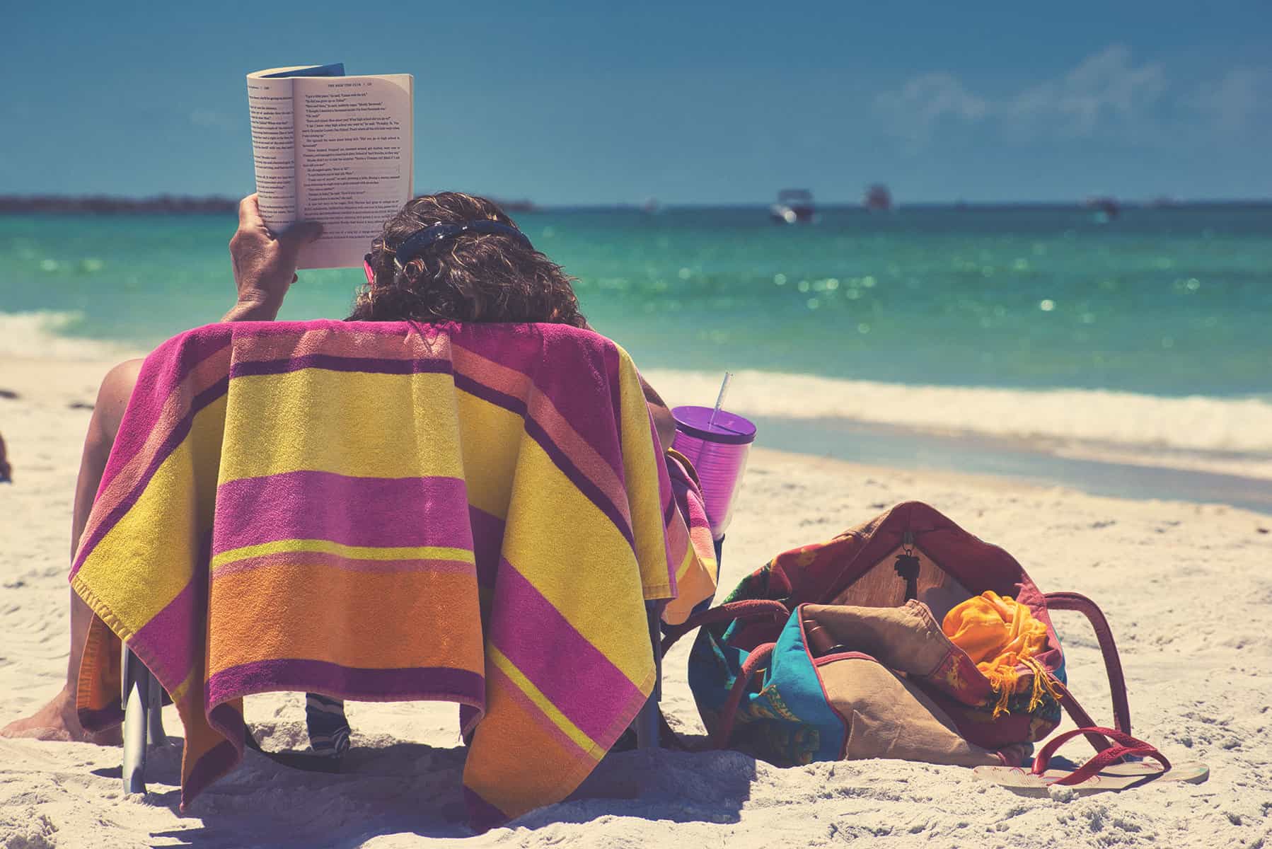 A person sitting on a beach chair, covered with a cozy towel, reading a book and enjoying the beach.