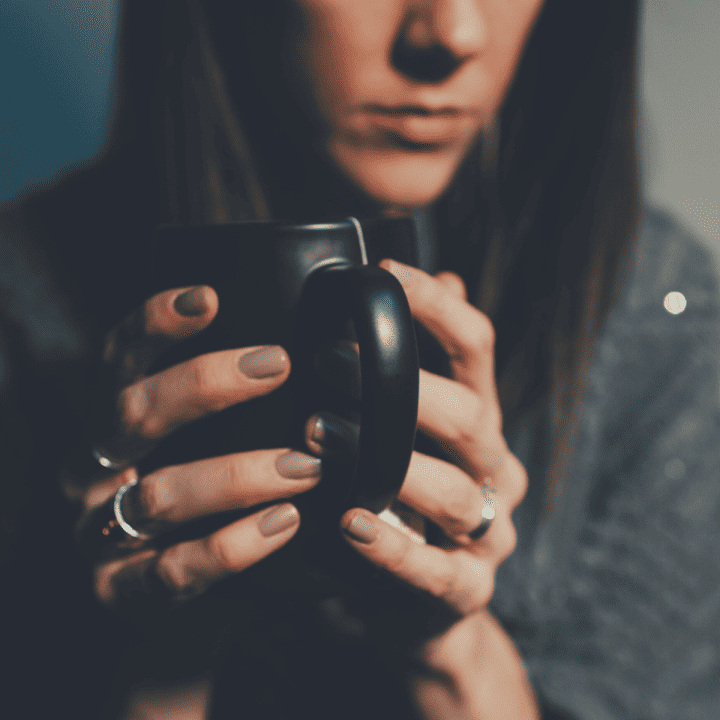A somber woman grasping a hot mug of tea with both hands wondering, "Why is my life falling apart?"