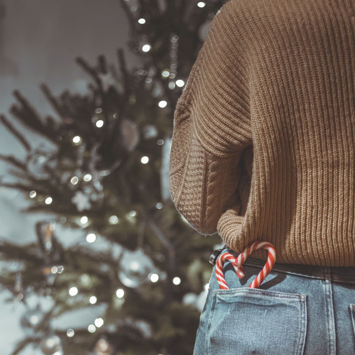 A woman enjoying the JOMO, standing in front of a Christmas tree with candy canes in her back jean pocket.