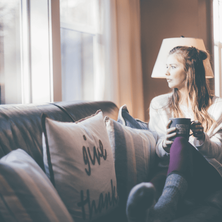 A woman with an interest-based nervous system sitting on a couch with a cup of coffee looking out the window frustrated by her lack of motivation.