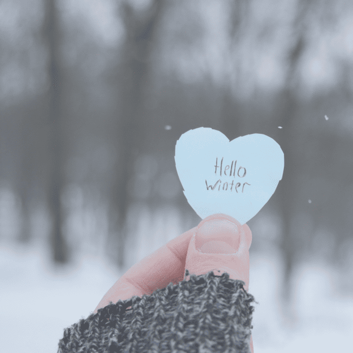 Woman holding a cutout heart with the words "hello winter" written on it.