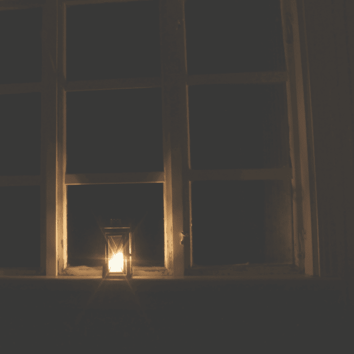 A lit candle sitting in a dark window.