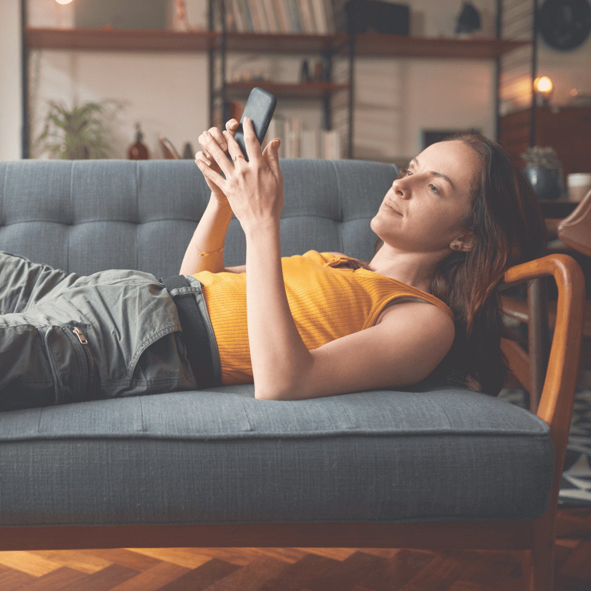 A woman lying on a couch struggling with the FOMO as she scrolls on her phone.